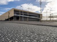 a long building on a side walk with brick in front of it and two people walking around the walkway