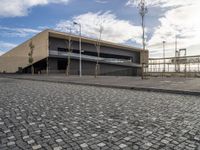 a long building on a side walk with brick in front of it and two people walking around the walkway