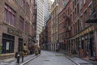 a cobble stone street is shown near tall buildings and fire escape ladders is shown in the background