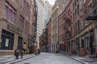 a cobble stone street is shown near tall buildings and fire escape ladders is shown in the background