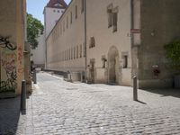 a cobblestone road next to some buildings and some trees, and a white fire hydrant
