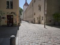 a cobblestone road next to some buildings and some trees, and a white fire hydrant