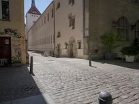 a cobblestone road next to some buildings and some trees, and a white fire hydrant