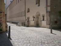 a cobblestone road next to some buildings and some trees, and a white fire hydrant