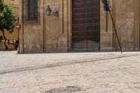 a person walks down a cobbled road past the old building on which a woman is sitting