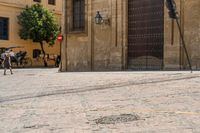 a person walks down a cobbled road past the old building on which a woman is sitting