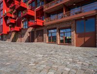 a cobbled sidewalk outside of a very tall red building with balconies and windows