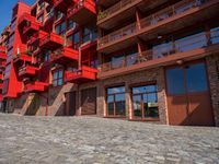 a cobbled sidewalk outside of a very tall red building with balconies and windows