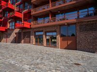 a cobbled sidewalk outside of a very tall red building with balconies and windows