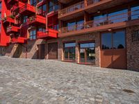 a cobbled sidewalk outside of a very tall red building with balconies and windows