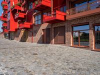 a cobbled sidewalk outside of a very tall red building with balconies and windows