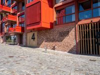 a cobbled sidewalk outside of a very tall red building with balconies and windows