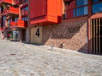 a cobbled sidewalk outside of a very tall red building with balconies and windows