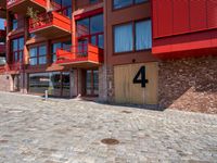 a cobbled sidewalk outside of a very tall red building with balconies and windows