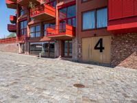 a cobbled sidewalk outside of a very tall red building with balconies and windows