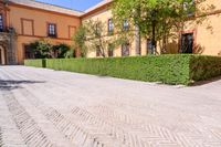 a cobbled sidewalk in front of a beautiful home with windows and bushes surrounding it