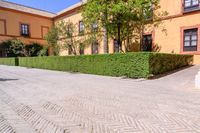 a cobbled sidewalk in front of a beautiful home with windows and bushes surrounding it