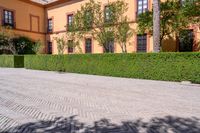 a cobbled sidewalk in front of a beautiful home with windows and bushes surrounding it