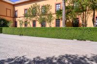 a cobbled sidewalk in front of a beautiful home with windows and bushes surrounding it