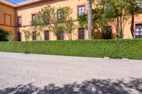 a cobbled sidewalk in front of a beautiful home with windows and bushes surrounding it