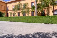 a cobbled sidewalk in front of a beautiful home with windows and bushes surrounding it