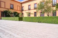 a cobbled sidewalk in front of a beautiful home with windows and bushes surrounding it