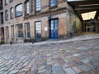 a cobbled - in parking area on the side of a brick building with blue doors