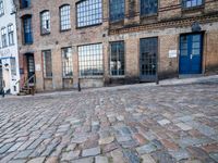 a cobbled - in parking area on the side of a brick building with blue doors