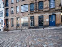 a cobbled - in parking area on the side of a brick building with blue doors