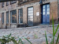 a cobbled - in parking area on the side of a brick building with blue doors