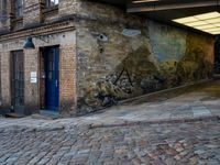 a cobbled - in parking area on the side of a brick building with blue doors