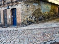 a cobbled - in parking area on the side of a brick building with blue doors