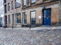 a cobbled - in parking area on the side of a brick building with blue doors