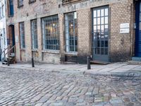 a cobbled - in parking area on the side of a brick building with blue doors