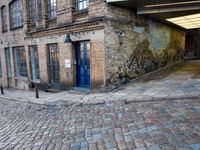 a cobbled - in parking area on the side of a brick building with blue doors