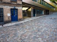 a cobbled - in parking area on the side of a brick building with blue doors