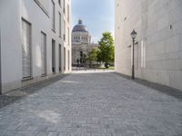 a walkway with an outside light next to some buildings in a city area with cobblestone and trees