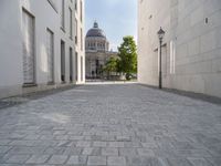 a walkway with an outside light next to some buildings in a city area with cobblestone and trees