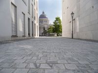 a walkway with an outside light next to some buildings in a city area with cobblestone and trees