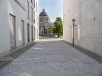 a walkway with an outside light next to some buildings in a city area with cobblestone and trees