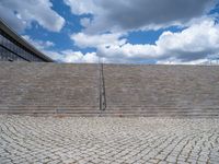 a person on a bike walking through a stone building entrance, in front of an enormous glass wall and stairs