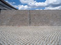 a person on a bike walking through a stone building entrance, in front of an enormous glass wall and stairs