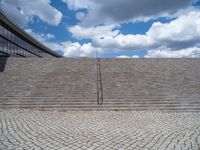 a person on a bike walking through a stone building entrance, in front of an enormous glass wall and stairs