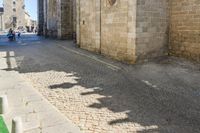 the shadow of a clock is on a cobblestone street near a building with two people