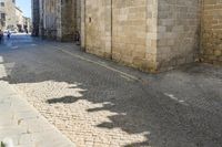 the shadow of a clock is on a cobblestone street near a building with two people