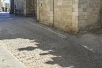 the shadow of a clock is on a cobblestone street near a building with two people