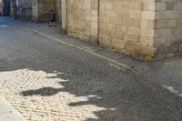 the shadow of a clock is on a cobblestone street near a building with two people