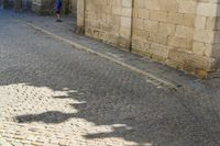 the shadow of a clock is on a cobblestone street near a building with two people