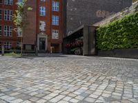 a green shrub near a gray building and a brick walkway with a bicycle rack in it