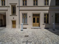 a green shrub near a gray building and a brick walkway with a bicycle rack in it